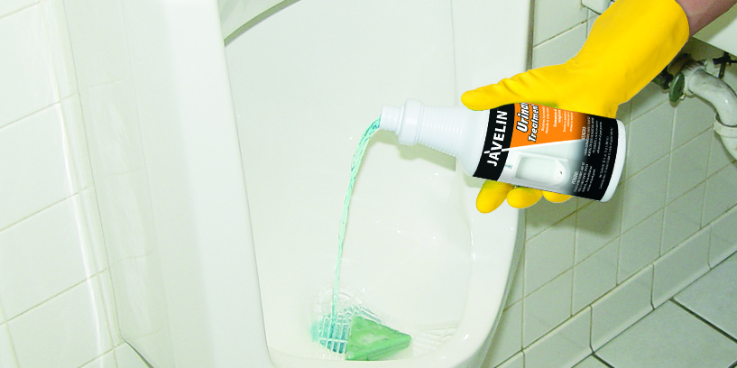 Person applying Javelin Urinal Treatment into a urinal to dissolve uric salt and restore proper drainage in a commercial restroom